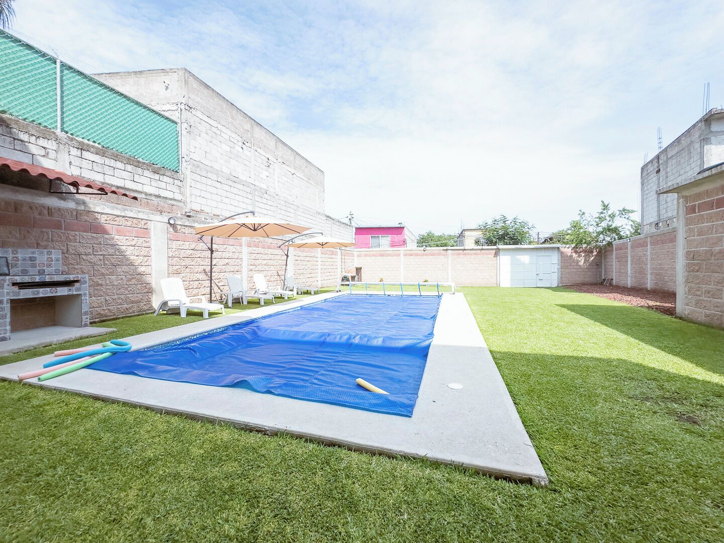 Un patio trasero con piscina, zona de barbacoa y césped.
