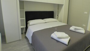 A modern hotel room with a bed, white linens, a dark headboard, and a built-in shelf above the bed. - B&B - Il Terrazzo da Gregorio - Room 2 (Roma)