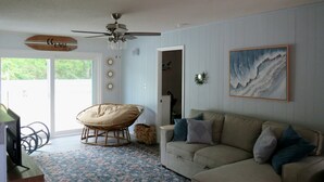 Ein Wohnzimmer mit einer Couch, einem Sessel, einem Deckenventilator, einem Gemälde und einem gemusterten Teppich.