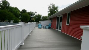 Eine überdachte Terrasse mit weißer Geländer, ein rotes Gebäude und zwei blaue Stühle.