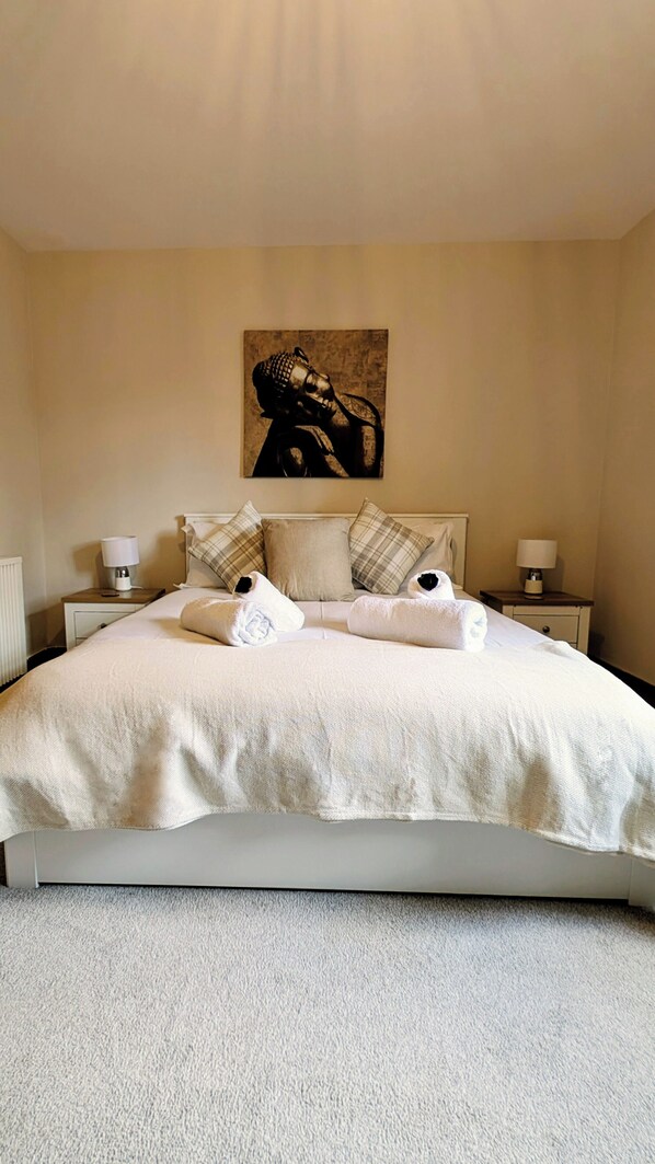 A neatly made bed with two towels, a headboard, and a painting on the wall.