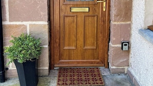 A wooden door with a glass panel, a brass handle, and a small brass knocker. There is a potted plant to the left and a doormat in front of the door.