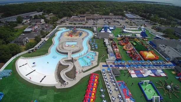 An aerial view of a water park with a winding pool, various water slides, and inflatable play areas.