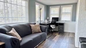 A modern living room with a dark grey sofa, a desk with a computer, and a chair.