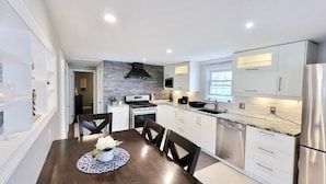 A modern kitchen with white cabinetry, a central island, stainless steel appliances, and a dining area with a table and chairs.