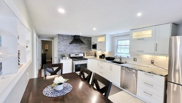 A modern kitchen with white cabinetry, a central island, stainless steel appliances, and a dining area with a table and chairs.