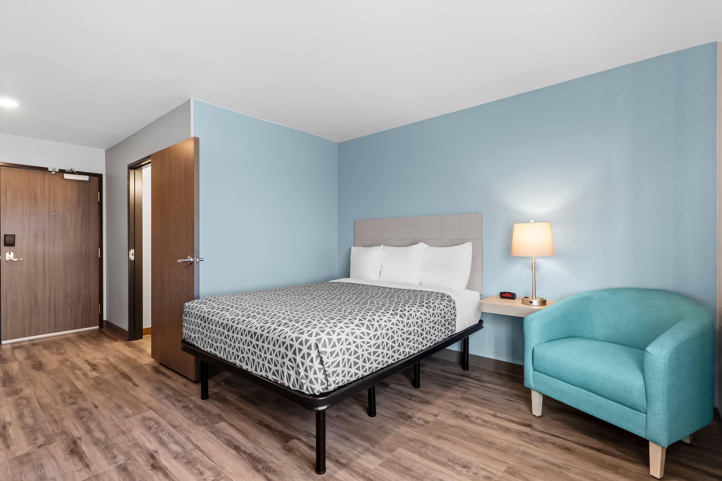 Une chambre d’hôtel avec un lit, une table de chevet, une lampe, une chaise et une porte en bois.