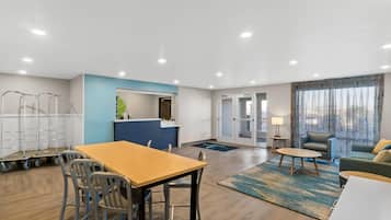 Una habitación de hotel moderna con zona de comedor, kitchenette y una sala de estar con sofá y sillón.