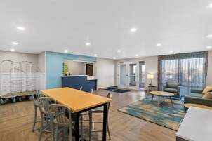 Una habitación de hotel moderna con zona de comedor, kitchenette y una sala de estar con sofá y sillón.