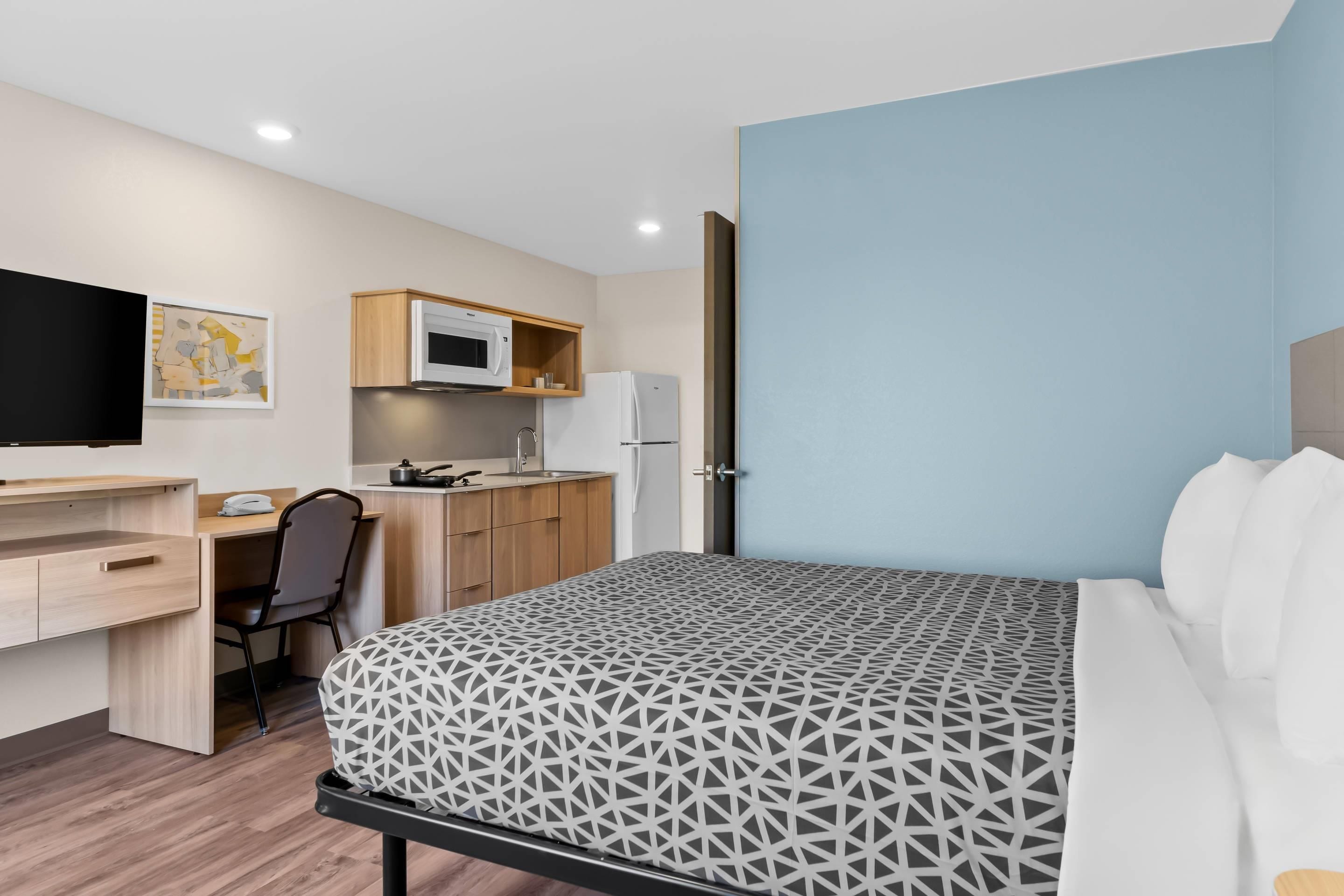 A hotel room with a bed, a desk with a chair, a television, a microwave, and a refrigerator.