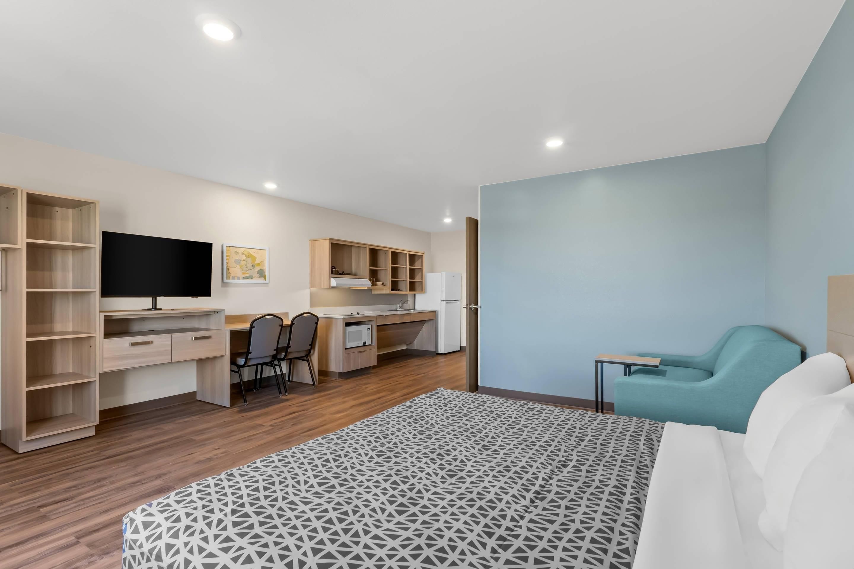 A modern bedroom with a bed, a desk, a chair, and a television.