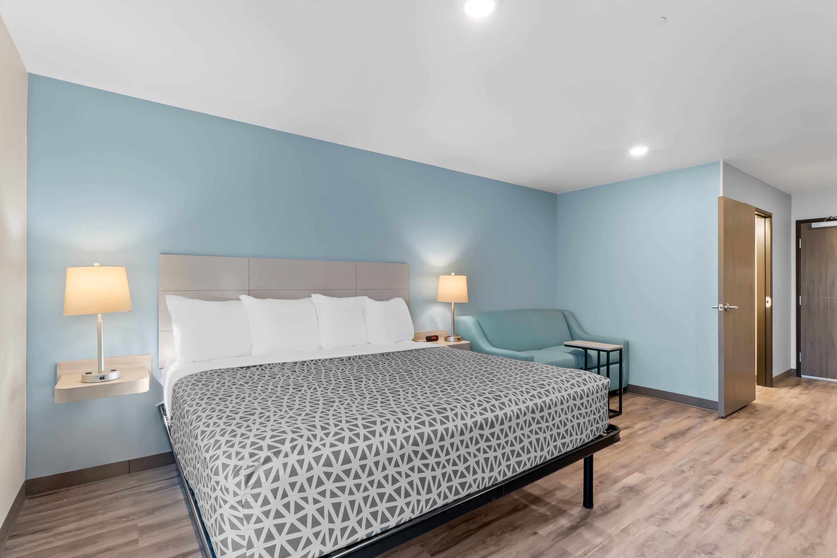 A modern bedroom with a large bed, bedside lamps, a chair, and a wardrobe.