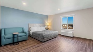 A bedroom with a bed, a sofa, a nightstand, a window with a view, and a radiator. - WoodSpring Suites Centennial - Denver Tech Center (Centennial)