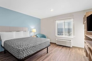 A hotel room with a bed, a desk, a chair, a TV, and a window with blinds. - WoodSpring Suites Centennial - Denver Tech Center (Centennial)