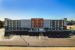 A multi-story hotel with a central entrance, a parking lot, and a clear sky.