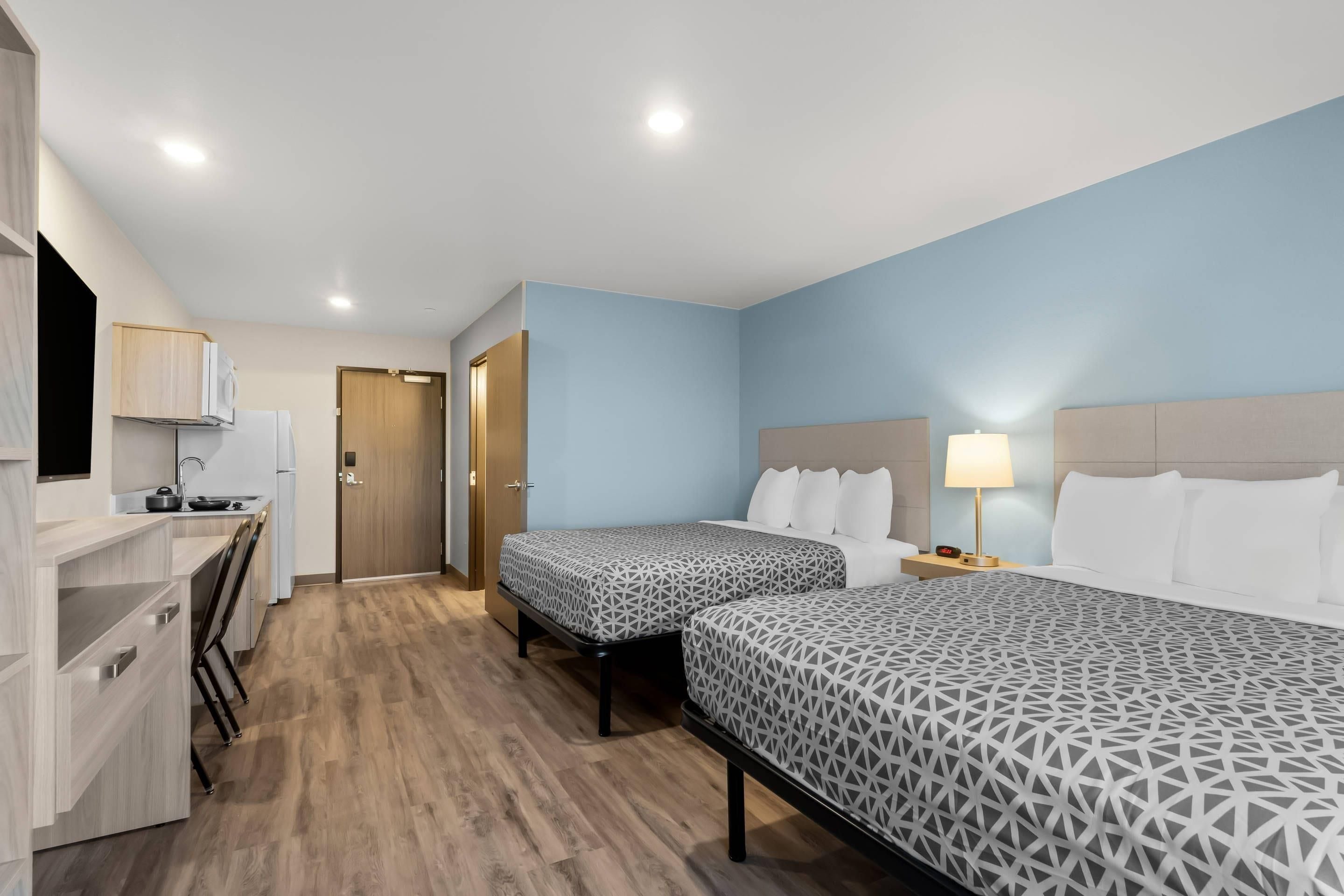 A hotel room with two beds, a desk, and a kitchenette.