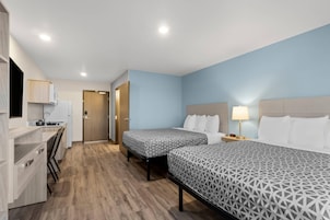A hotel room with two beds, a desk, and a kitchenette.