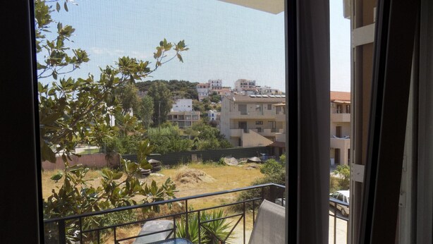 A balcony with a metal railing, a chair, and a view of a residential area with houses and trees. - Central Cute 2Bd Balcony apt in Skiathos (Skiathos)