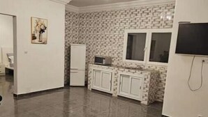 Una cocina moderna con piso de baldosas, gabinetes blancos, un microondas integrado y un televisor montado en la pared.