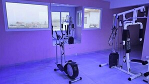 Un gimnasio con equipo de ejercicio, ventanas amplias y vistas a edificios.