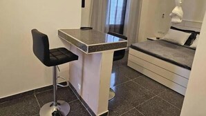 Habitación de hotel pequeña con cama, un escritorio y una silla, una ventana con cortinas y un dosel blanco sobre la cama.