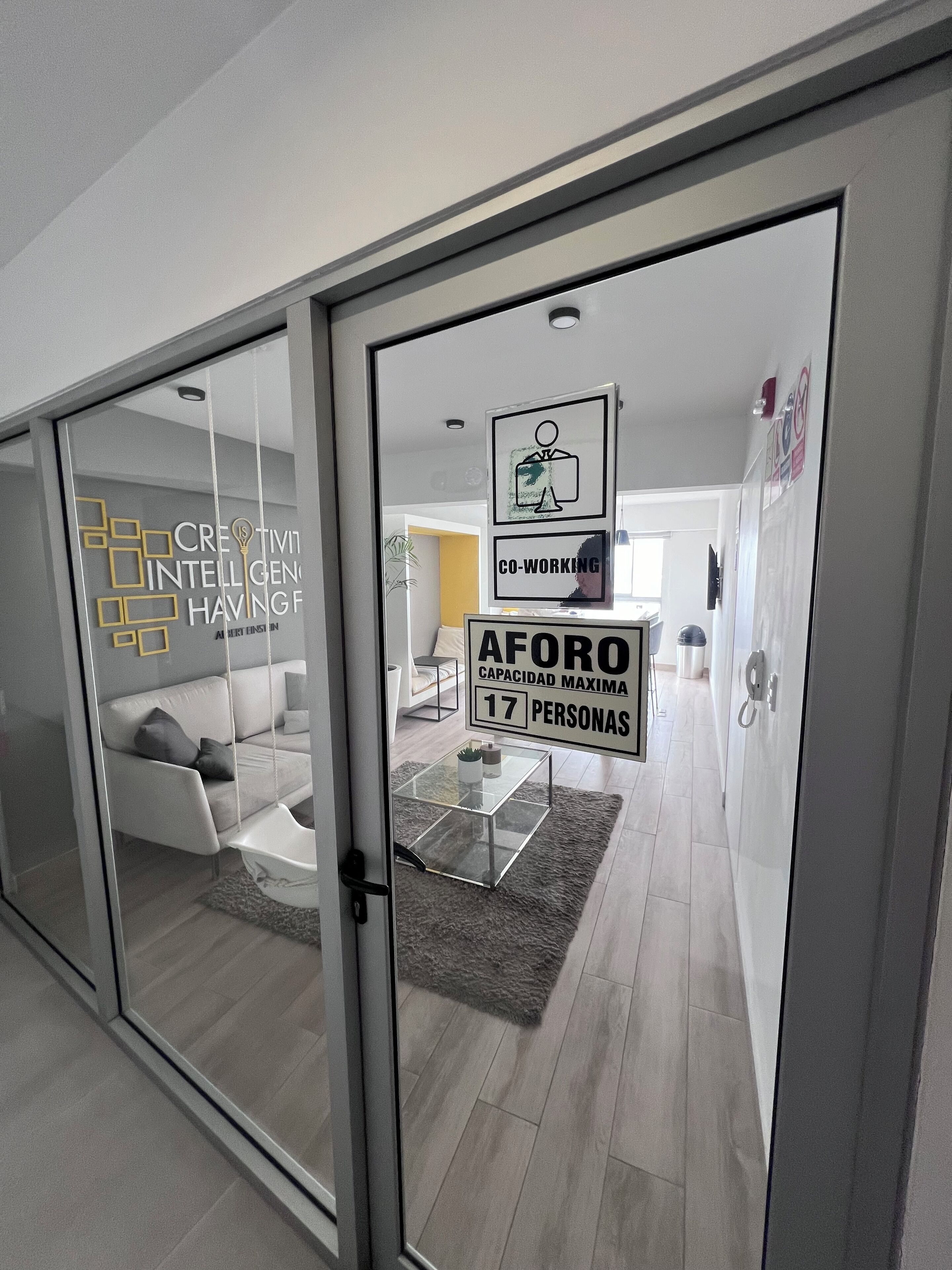 A modern office space with a glass door, a sign indicating a capacity of 17 people, and a logo for 'AFORO' with a capacity of maximum 17 persons.