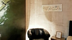 Ein Zimmer mit einem schwarzen Ledersessel, einem großen abstrakten Gemälde und einem kleinen Holztisch mit Bilderrahmen.