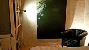Ein Schlafzimmer mit einem Bett, einem Sessel, einem Fenster mit Vorhängen und einem Wandbild.