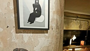 Ein rustikales Interieur mit einem gerahmten Kunstwerk, einer Bronzestatue und einem Korbwägelchen auf einem Tisch.
