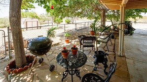 A covered patio area with a stone floor, outdoor furniture, a barbecue grill, and potted plants. - Spacious Route 66 retreat. Golf Course. Pet Friendly. Grand Canyon and Vegas. (Kingman)