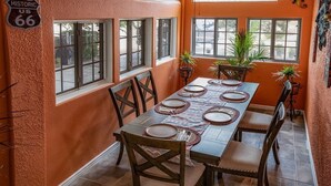 A dining area with a long table set for six, surrounded by chairs, with windows and plants. - Spacious Route 66 retreat. Golf Course. Pet Friendly. Grand Canyon and Vegas. (Kingman)
