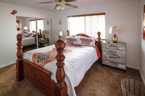 A bedroom with a wooden four-poster bed, a nightstand with a lamp, a dresser, and a mirror. - Spacious Route 66 retreat. Golf Course. Pet Friendly. Grand Canyon and Vegas. (Kingman)