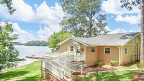 A single-story house with a deck overlooking a lake, surrounded by trees. - NEW! 3 bedroom lakefront home with wheelchair accessibility, sleeps 8! (Dadeville)