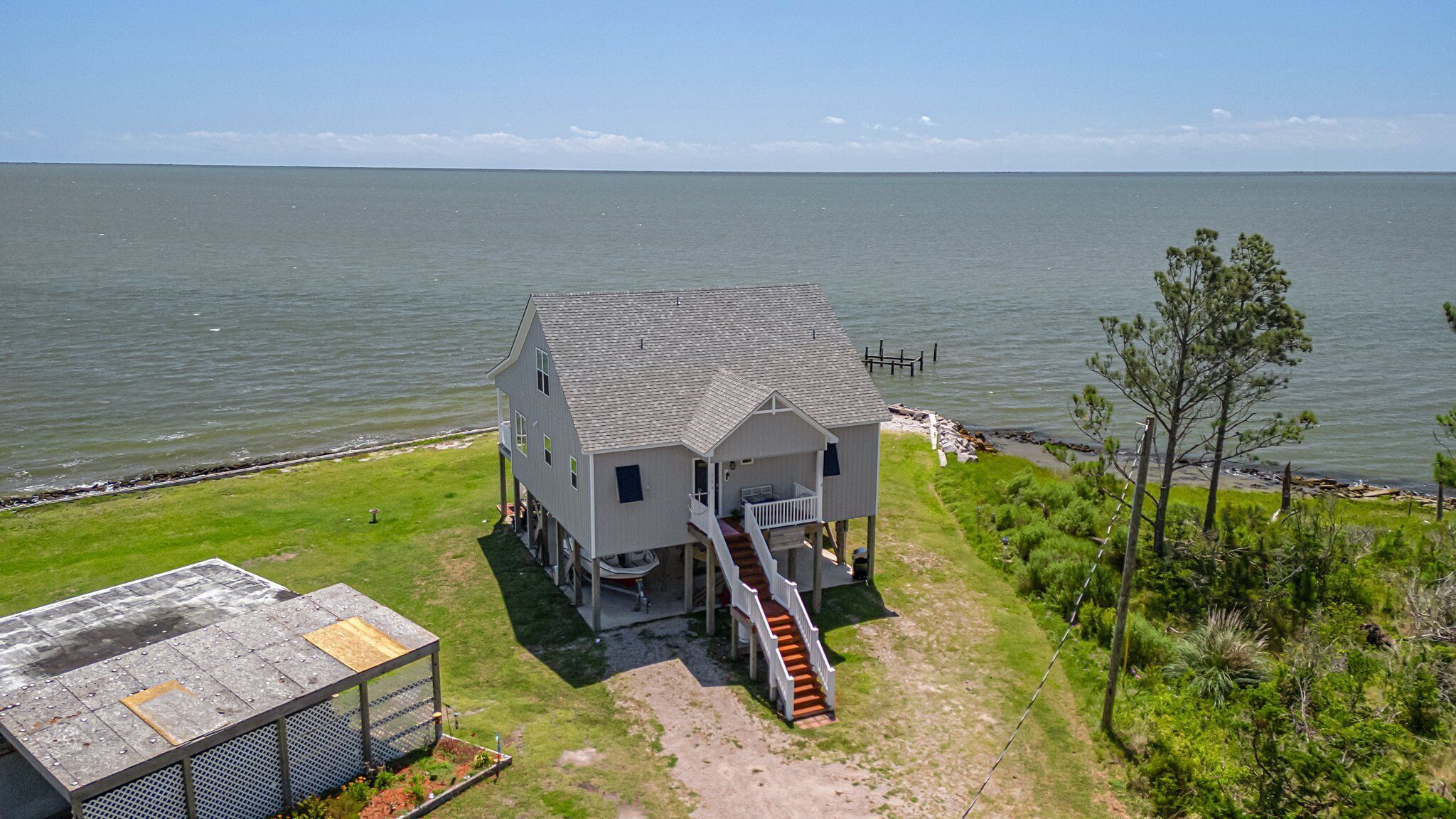 A two-story house with a porch and a staircase leading to the second floor, situated by a body of water.