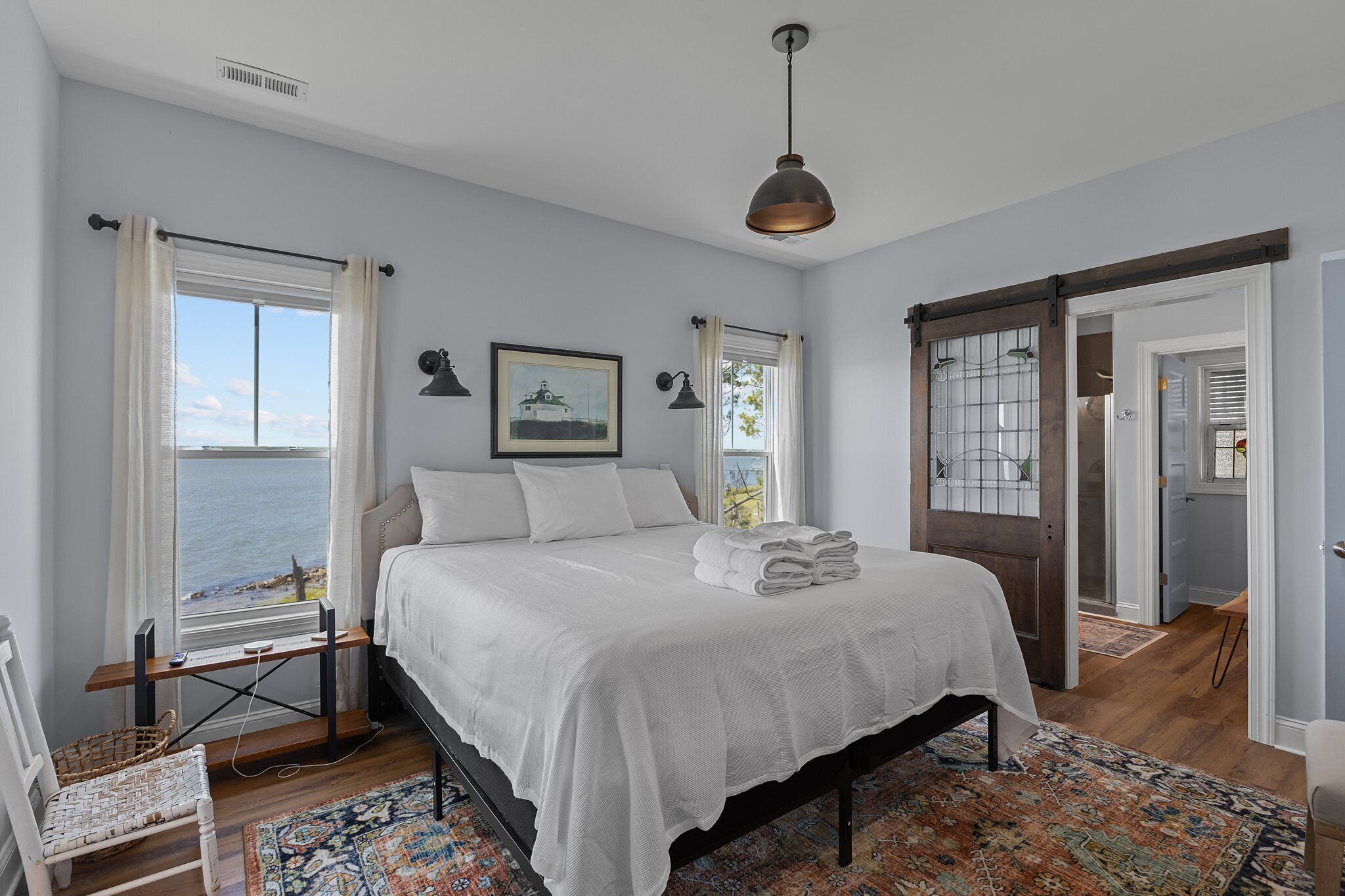 A bedroom with a large bed, a view of the sea through a window, and a door leading to another room.