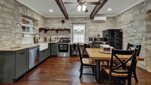 Una cocina con paredes de piedra, vigas de madera, una mesa de comedor con sillas y electrodomésticos modernos.