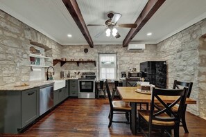 A kitchen with stone walls, wooden beams, a dining table with chairs, and modern appliances.