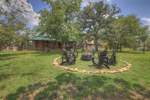 A rustic outdoor seating area with wooden chairs and a fire pit, surrounded by a stone border.