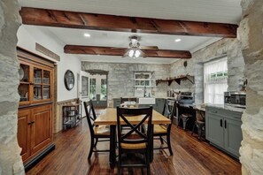 A rustic kitchen with wooden beams, stone walls, and a wooden dining table with chairs.