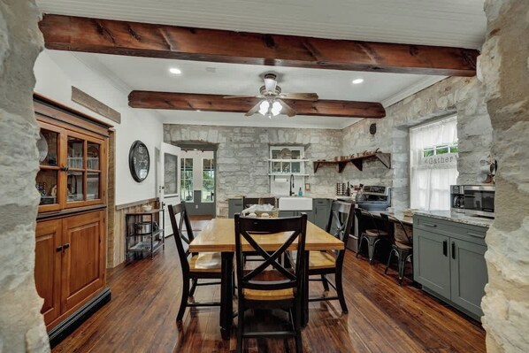 A rustic kitchen with wooden beams, stone walls, and a wooden dining table with chairs.