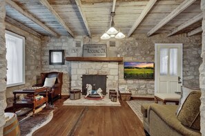Une pièce rustique avec un mur en pierre, un plancher en bois, une cheminée, un cheval à bascule et un tableau représentant un paysage.