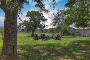 Un espace extérieur aménagé avec une table et des chaises, entouré d’arbres et d’un champ d’herbe.