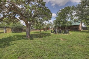A backyard with a lawn, a tree, a barbecue area, and a small building.