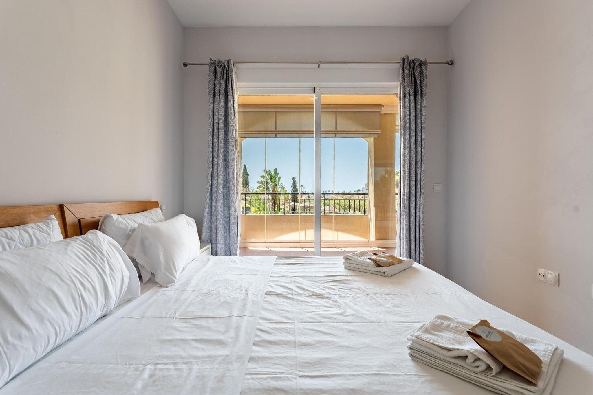 A hotel room with a large bed, a view of the outdoors through a sliding door, and a balcony with a railing.