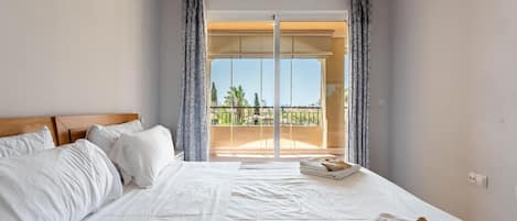 A hotel room with a large bed, a view of the outdoors through a sliding door, and a balcony with a railing.