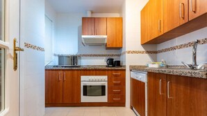 Een kleine keuken met houten kastjes, een inbouwoven, een koffiezetapparaat en een vaatwasser.