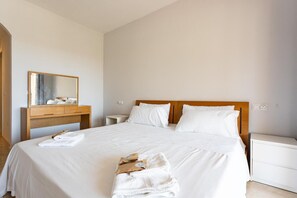 Een net opgemaakt bed met witte lakens, een houten hoofdbord en een nachtkastje met een lamp.