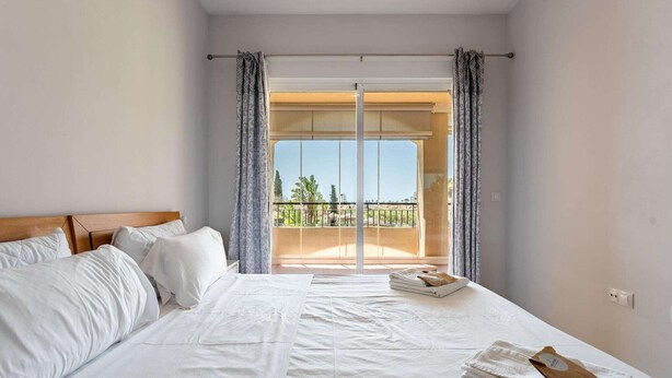 Een hotelkamer met een groot bed, een balkon met gordijnen en uitzicht op de omgeving.