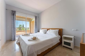 Een slaapkamer met een groot bed, een nachtkastje en uitzicht op een balkon.