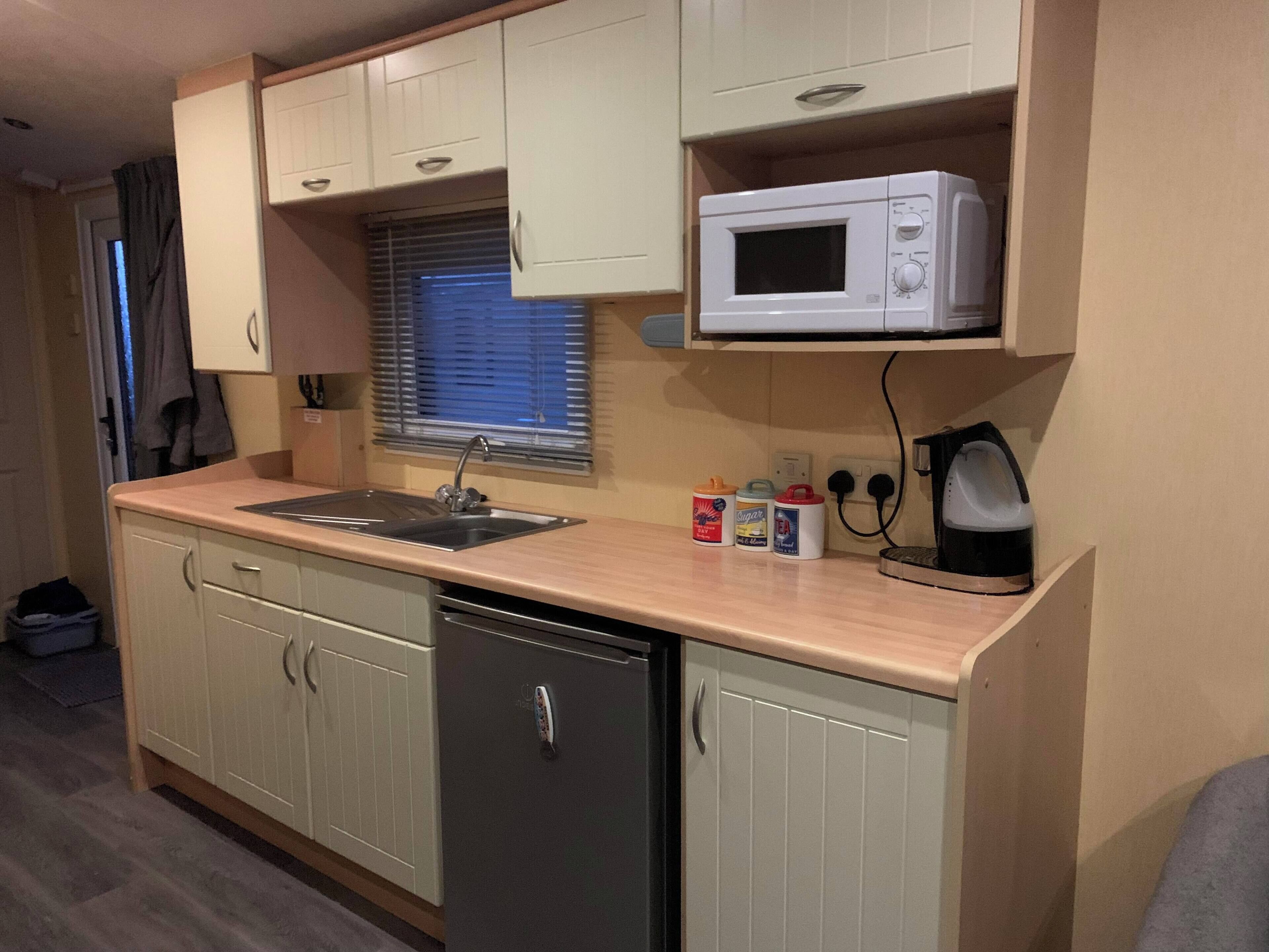 A compact kitchen with a sink, microwave, and kettle.